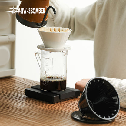 MHW-3BOMBER Meteor coffee dripper in use. White ceramic dripper on clear glass server. Black filter holder visible.