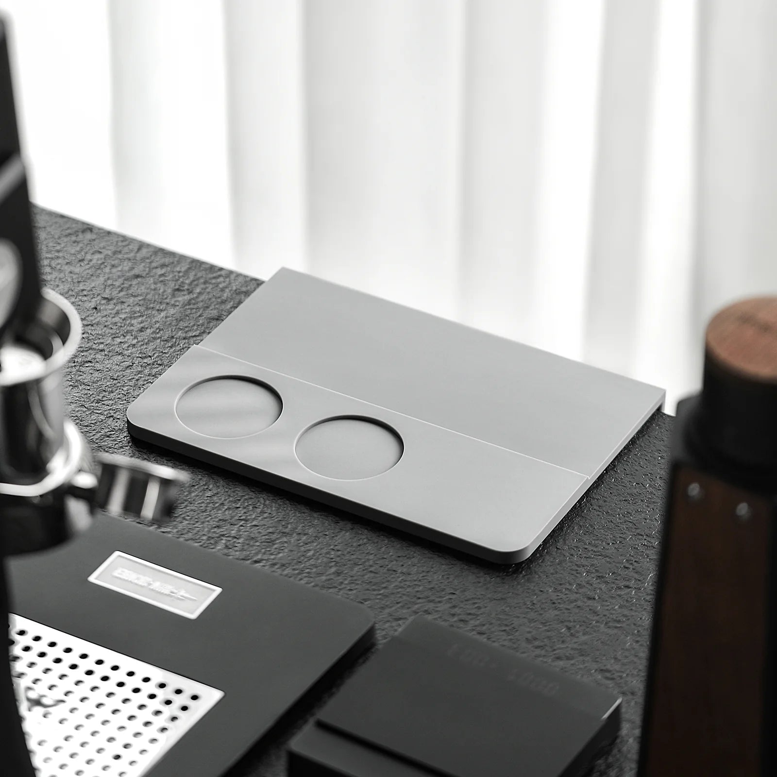 MHW-3BOMBER coffee tamper mat. Silicone pad, silver with two holes. On a counter.
