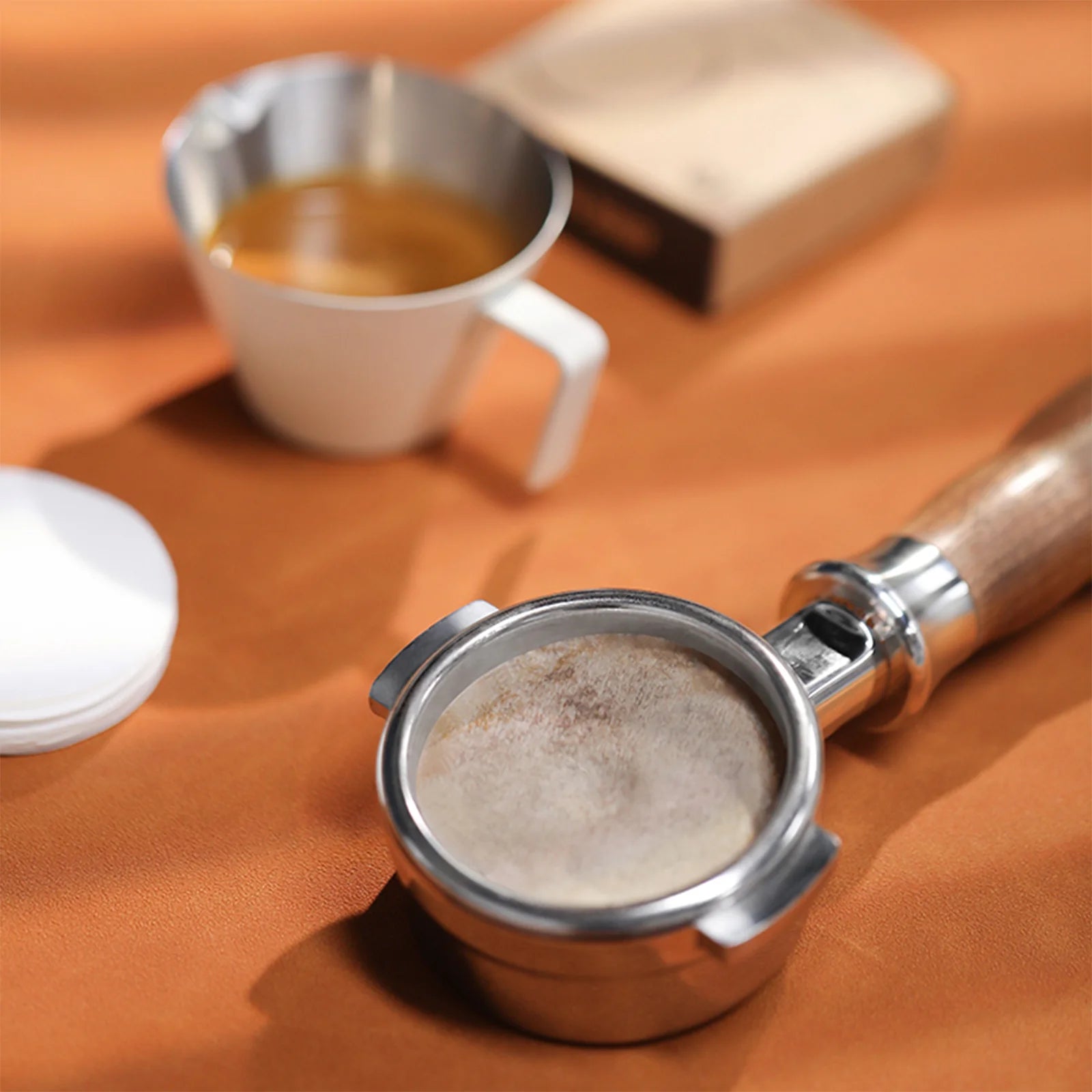 MHW-3BOMBER espresso setup: portafilter with filter paper, espresso, and coffee pack. 