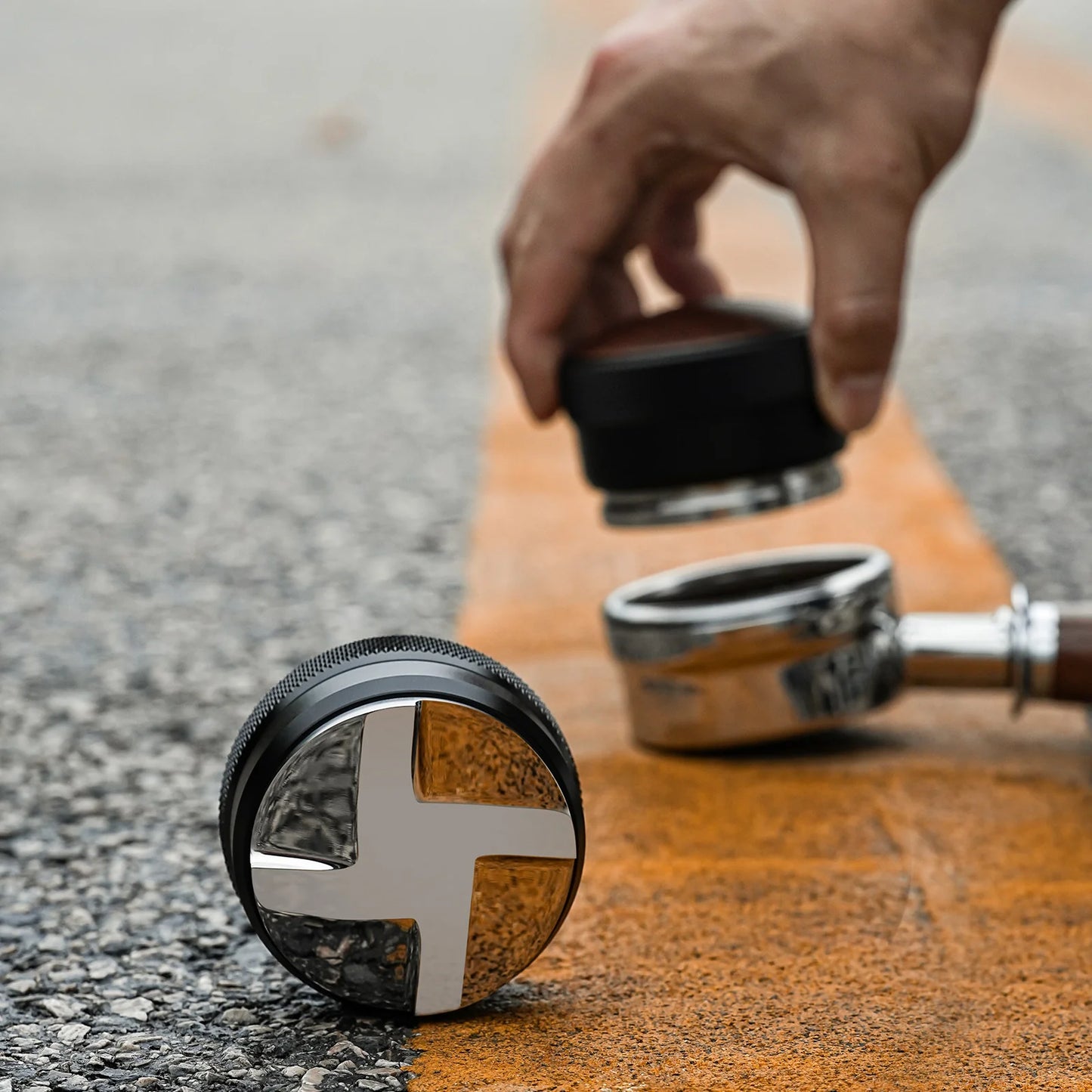 MHW-3BOMBER coffee distributor, black with silver cross design. Coffee tamper on a textured surface.