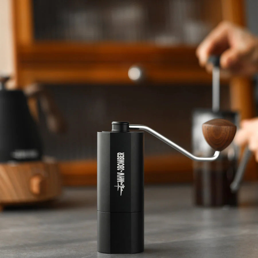MHW-3BOMBER black manual coffee grinder with wooden knob. Stainless steel burr visible. On counter.