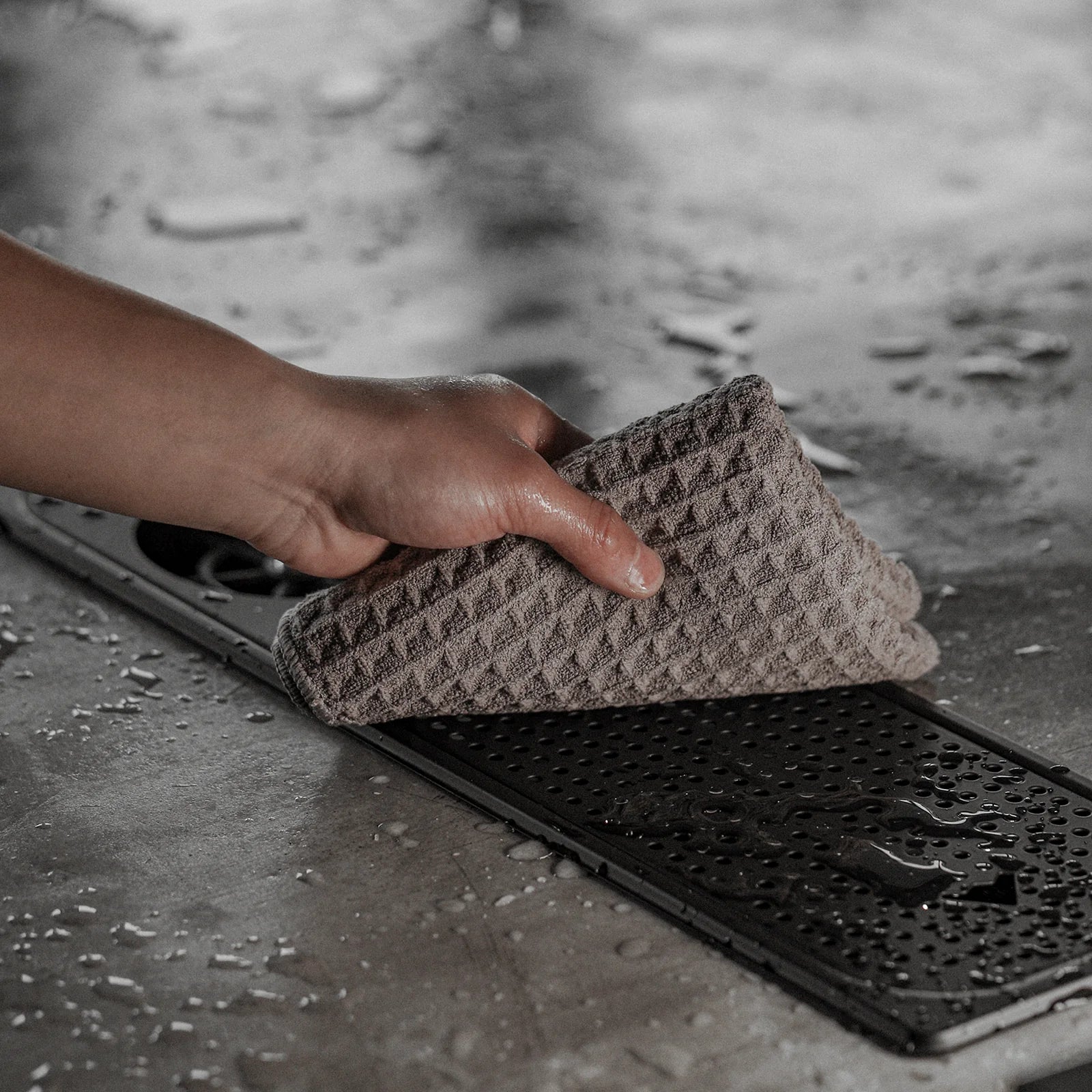 Barista Towel detail. Brown waffle weave texture wiping down a black drip tray. Daily Cleaning Essentials Kit item.