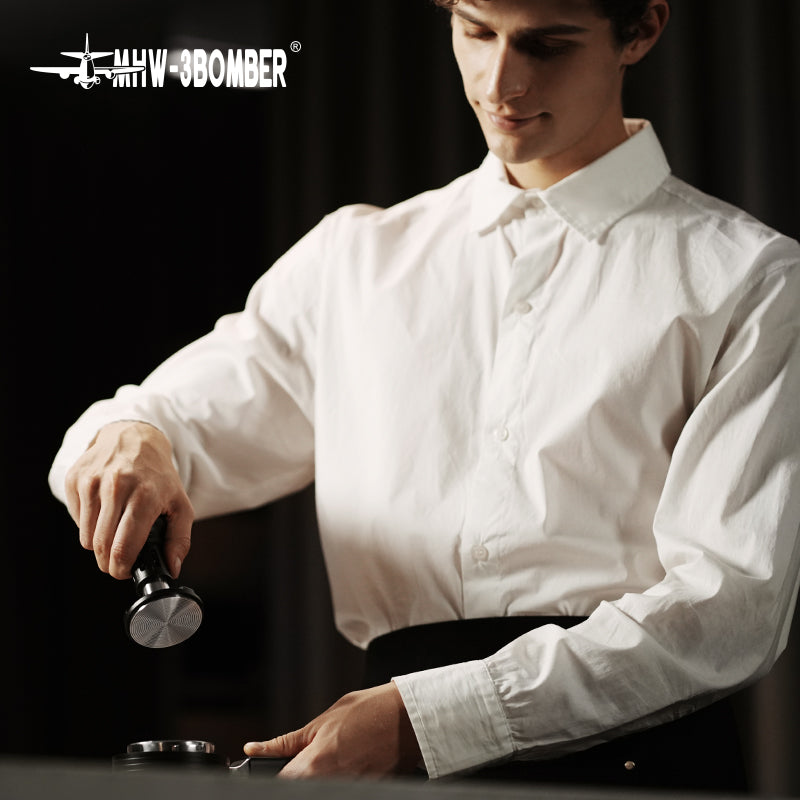 MHW-3BOMBER espresso tamper, 58mm, stainless steel base, black handle. Barista using the tool.