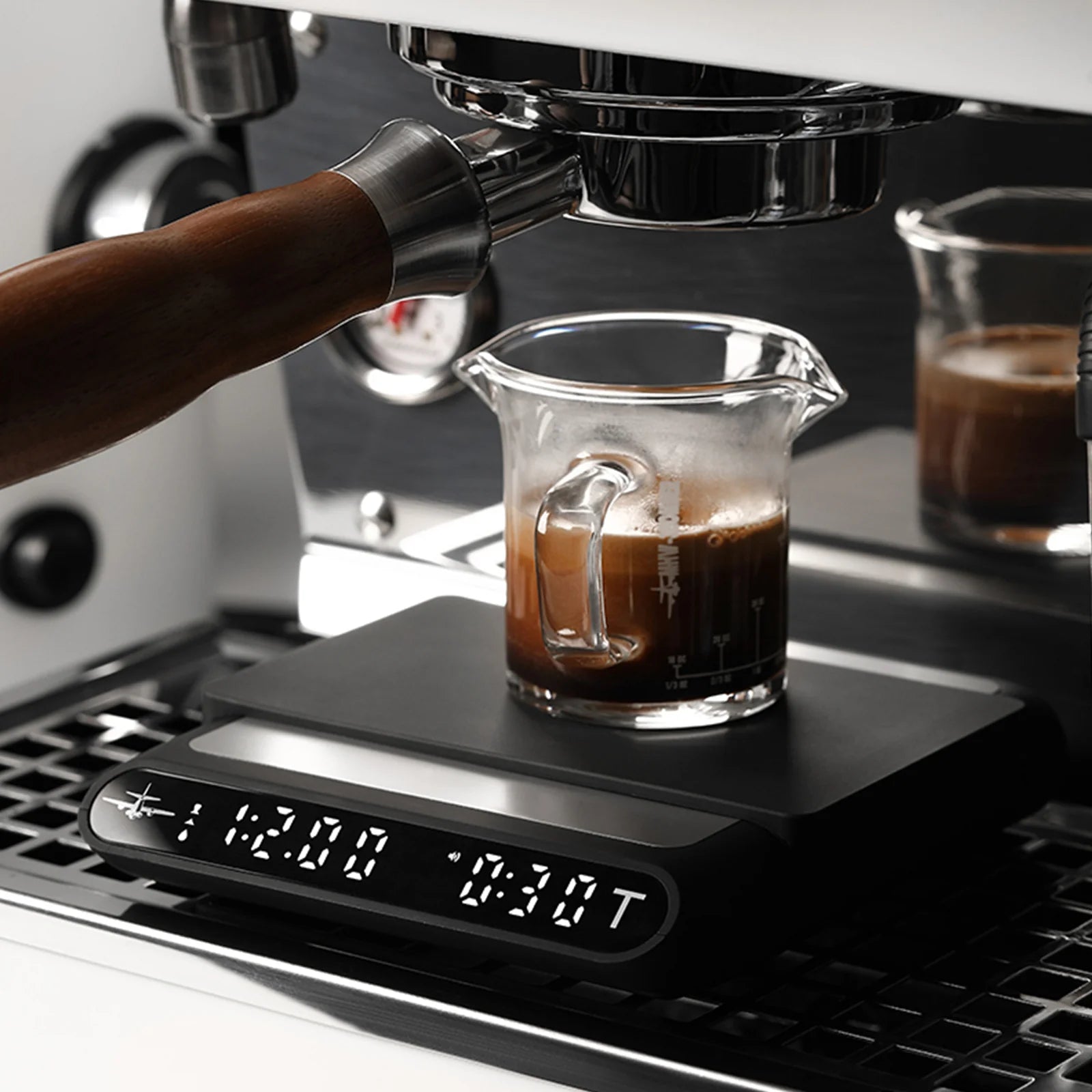MHW-3BOMBER black smart coffee scale with timer displaying stats as espresso brews into a glass measuring cup.