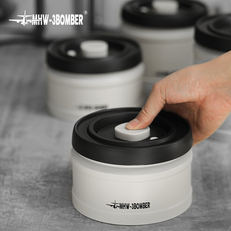 MHW-3BOMBER white coffee vacuum canister with black lid being pumped to seal; coffee storage.