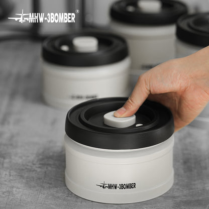 MHW-3BOMBER white coffee vacuum canister with black lid being pumped to seal; coffee storage.