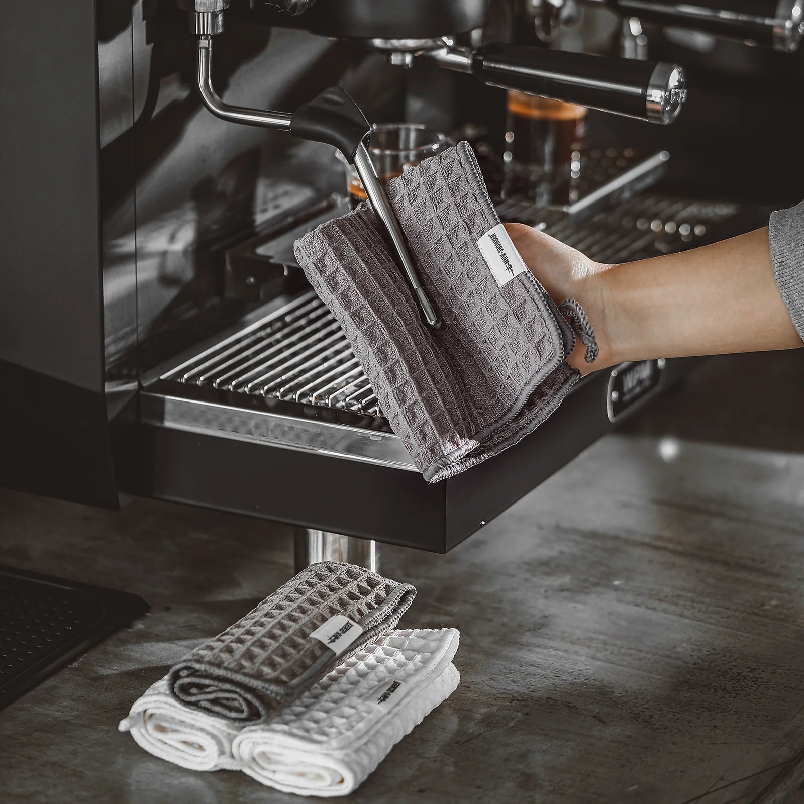 MHW-3BOMBER gray waffle towel used on espresso machine, plus stacked towels. Absorbent, quick-drying microfiber for baristas.