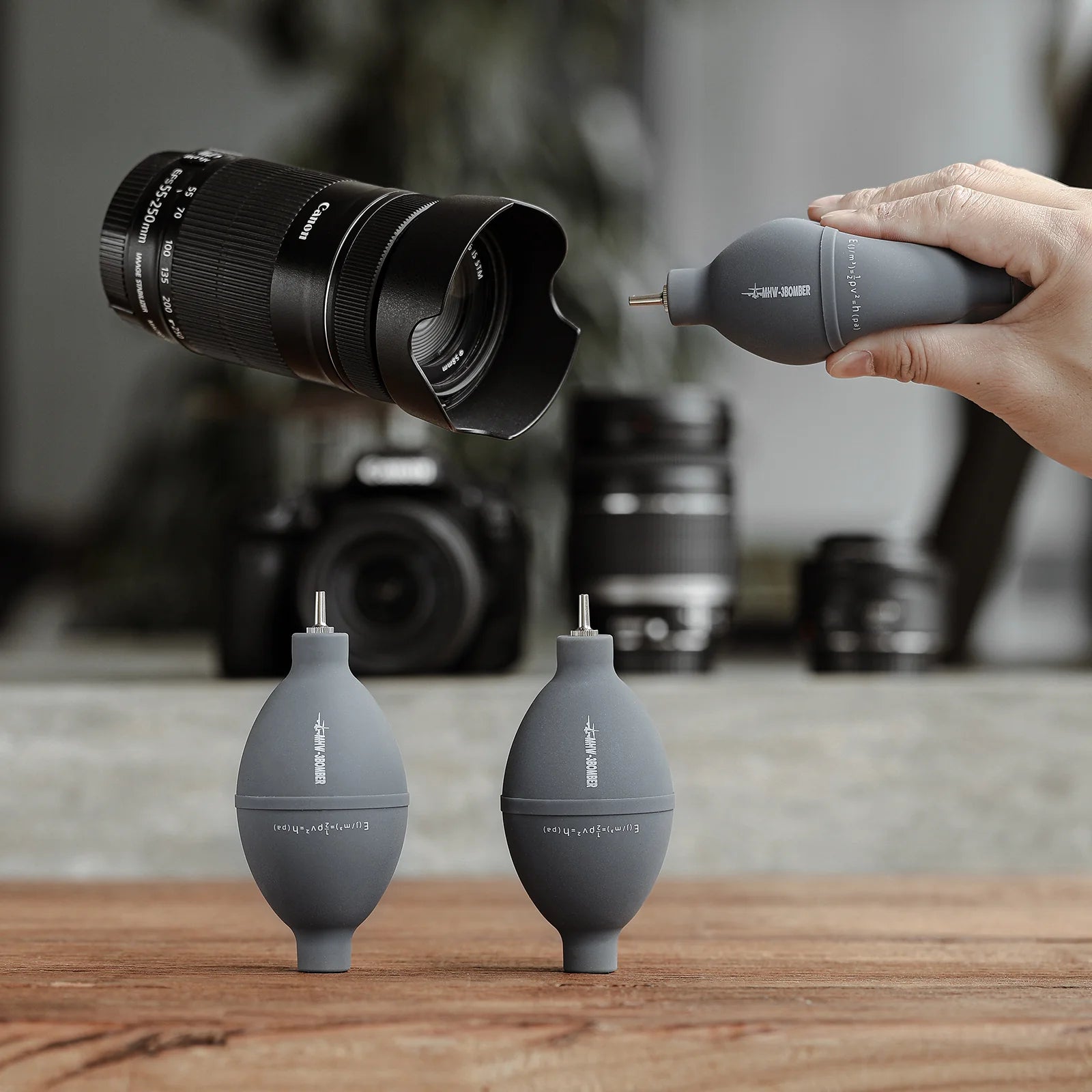 MHW-3BOMBER gray air blower for coffee/cameras. Silicone & stainless steel nozzle. Cleaning lenses, filters on wooden table.