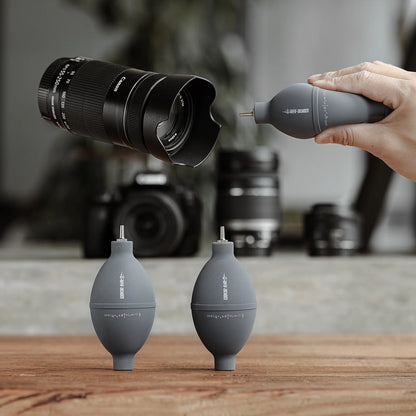 MHW-3BOMBER gray air blower for coffee/cameras. Silicone & stainless steel nozzle. Cleaning lenses, filters on wooden table.