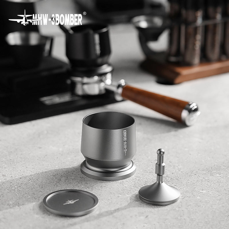 The MHW-3BOMBER Espresso Coffee Powder Dosing Funnel, with its silver finish and adjustable distributor handle, sits on the countertop. In the background, a coffee machine and wooden-handled tamper blur into view—essential tools for baristas honing their craft.