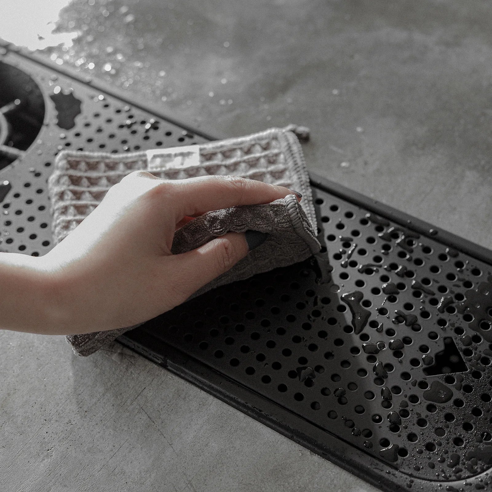 MHW-3BOMBER dark grey waffle towel being used to clean a black coffee maker part. Absorbent & reusable.