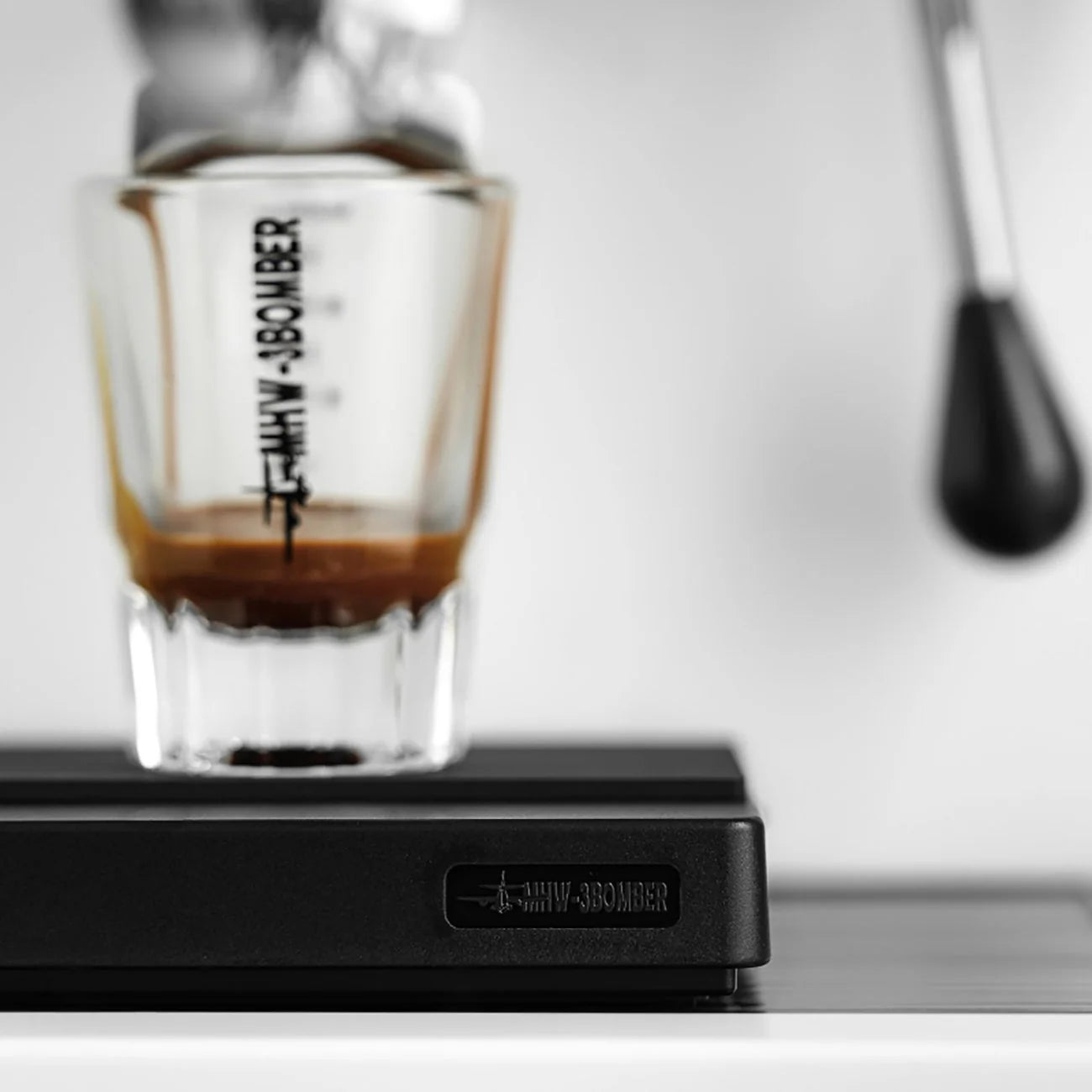 Close-up of an espresso being pulled from a machine, flowing into a glass on the MHW-3BOMBER Espresso Scale Cube Coffee Scale 2.0, featuring high precision and USB rechargeability. The background is out of focus, emphasizing the brewing process.