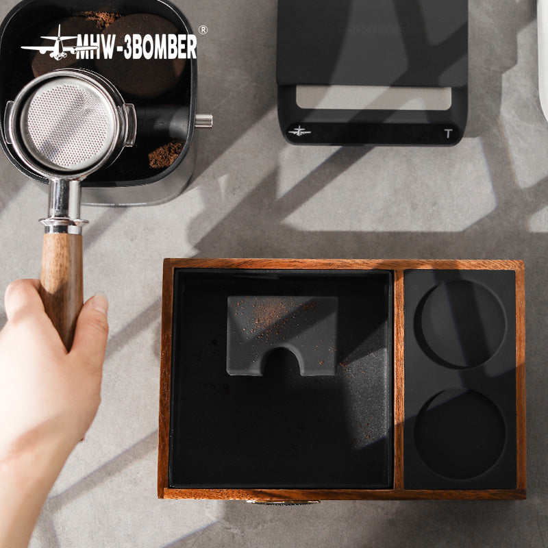MHW-3BOMBER espresso tamping station with wooden frame, black interior, portafilter, and espresso accessories.
