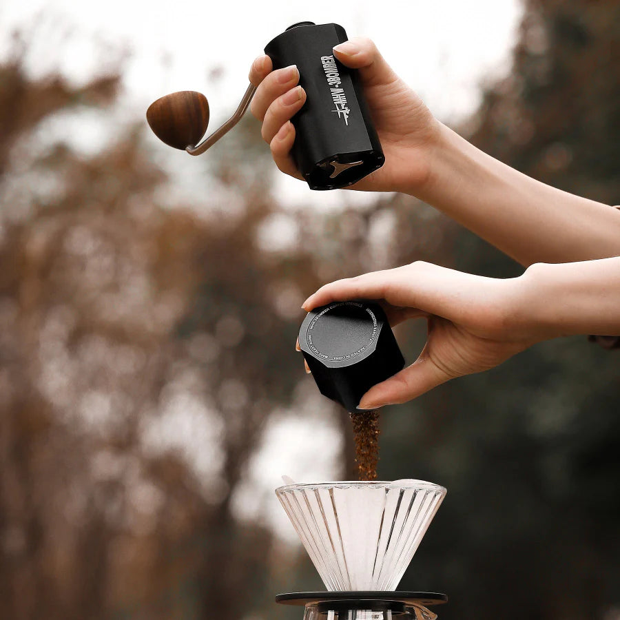 MHW-3BOMBER Adder V3 black manual coffee grinder in use, pouring grinds. Point-to-point adjustment, magnetic design.