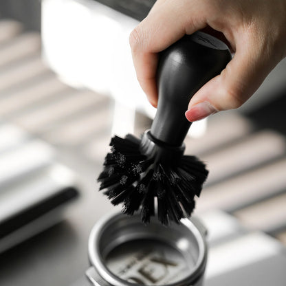 Portafilter cleaning brush in use. Black handle & bristles for espresso machine maintenance.