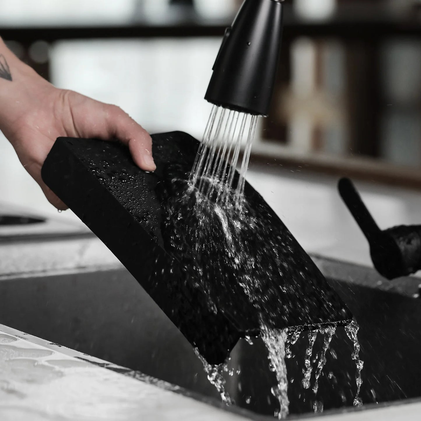 MHW-3BOMBER black silicone tamper mat being rinsed in a sink. Food-grade, non-toxic, and durable. Protects counters.