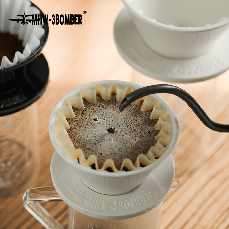 MHW-3BOMBER Meteor Dripper in use. White ceramic pour-over coffee maker shown with coffee and a water stream.