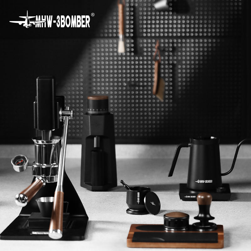 A minimalist coffee setup with a matte black and wood-accented manual espresso machine, coffee grinder, gooseneck kettle, tamper, and other barista accessories against a perforated wall. It includes the MHW-3BOMBER Espresso Coffee Powder Dosing Funnel by MHW-3BOMBER.