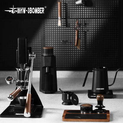 A minimalist coffee setup with a matte black and wood-accented manual espresso machine, coffee grinder, gooseneck kettle, tamper, and other barista accessories against a perforated wall. It includes the MHW-3BOMBER Espresso Coffee Powder Dosing Funnel by MHW-3BOMBER.
