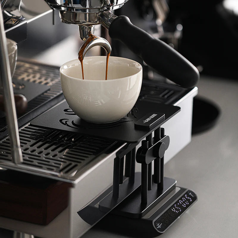 MHW-3BOMBER black coffee scale stand with adjustable height, silicone base, used with espresso machine on counter.