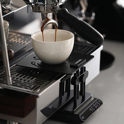 MHW-3BOMBER black coffee scale stand with adjustable height, silicone base, used with espresso machine on counter.