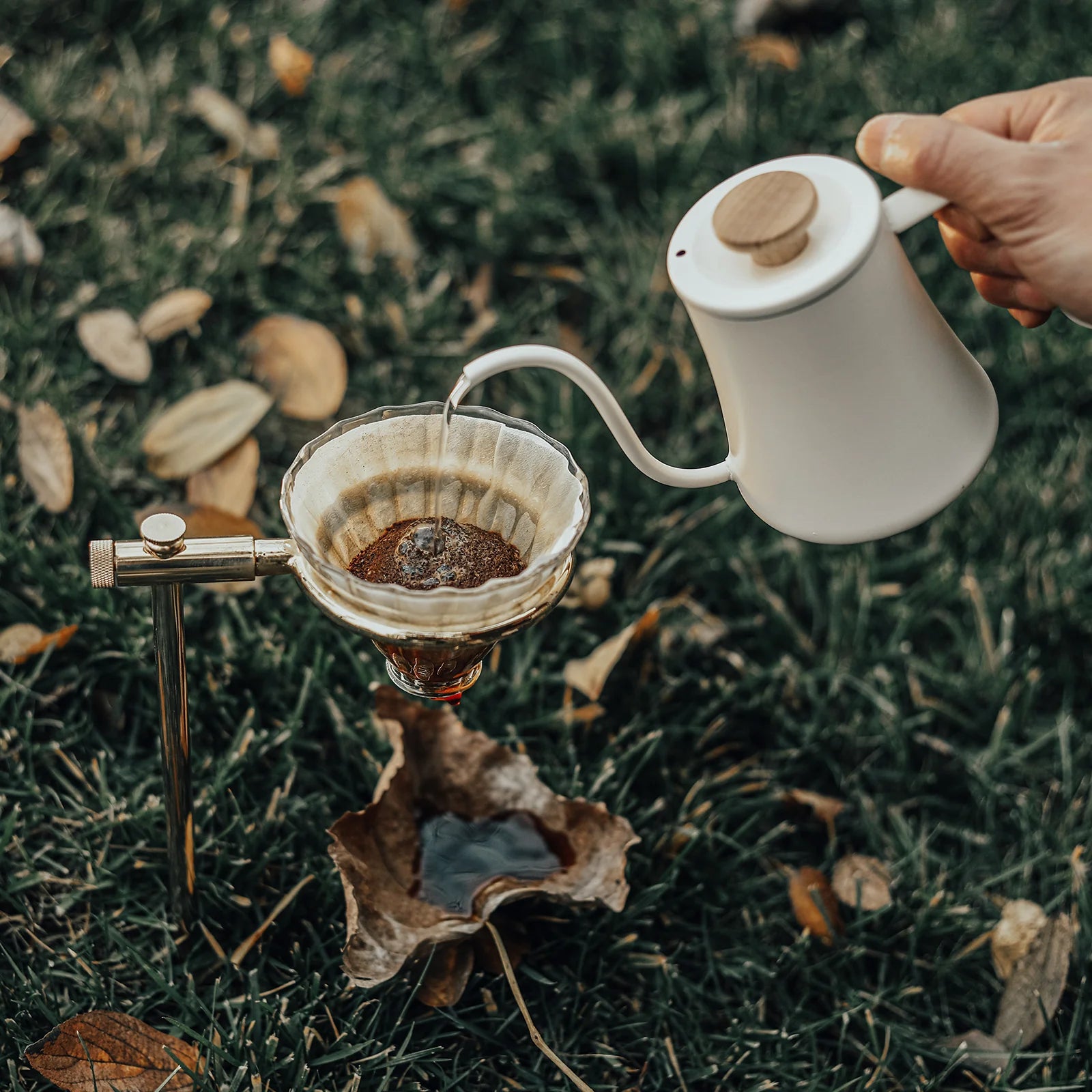 Pour-over coffee being brewed using a white kettle with a wood knob and a glass coffee filter and stand.