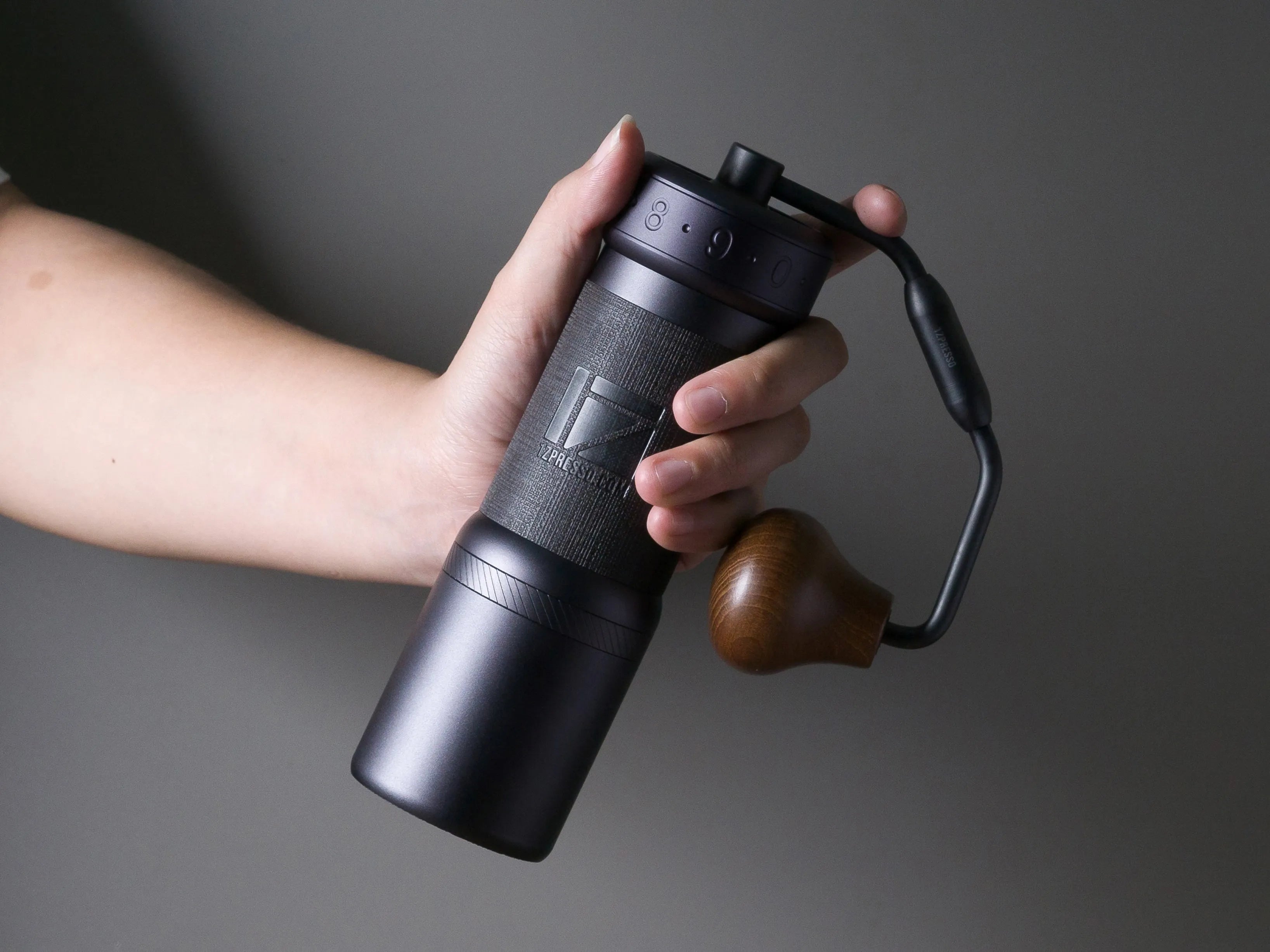 Hand holding a black portable coffee maker against a dark background
