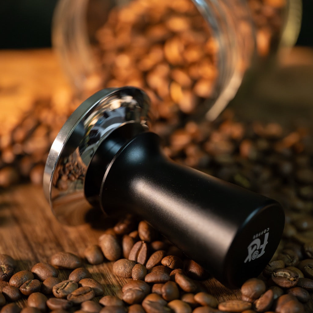 FIX COFFEE black tamper with silver base on coffee beans. Constant force, dual-spring mechanism, automatic spring reset.