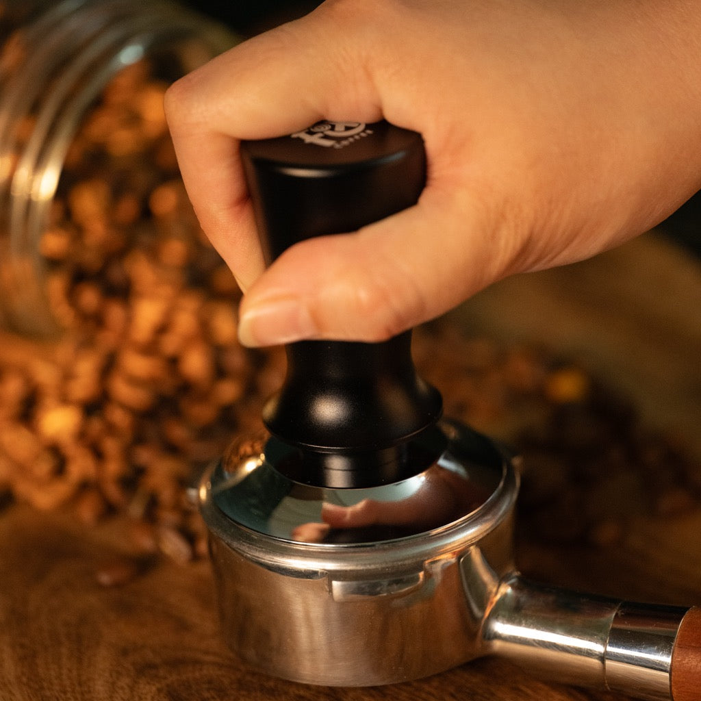 FIX COFFEE tamper being used on portafilter. Black handle, silver base. Constant force, spring activated leveling.