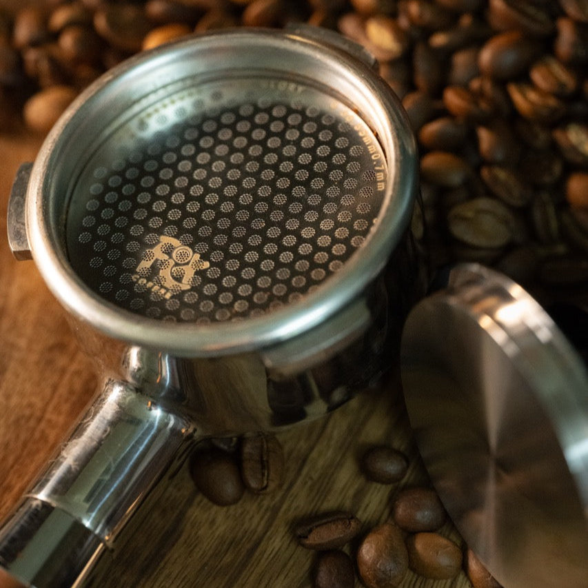 Fix Coffee 58mm espresso puck screen, titanium plated stainless steel, on wood with coffee beans. 
