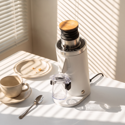DF54 V4 grinder in white with wooden lid on a sunlit table, dosing cup attached, beside a cup of coffee