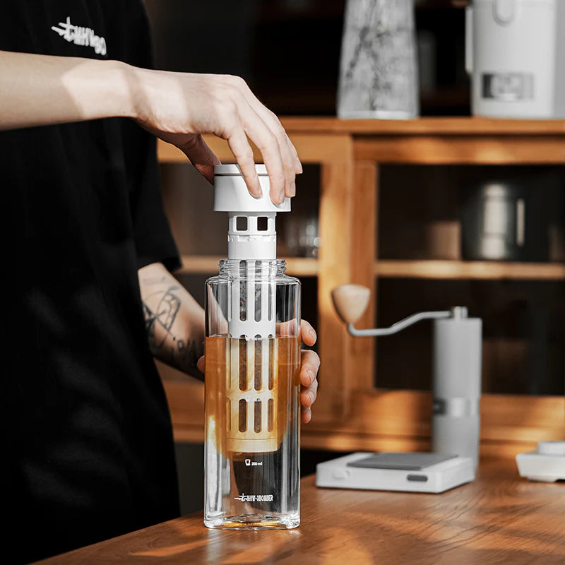 MHW-3BOMBER cold brew maker, clear Tritan bottle with white filter. User adding the filter. 600ml capacity. On wooden counter.