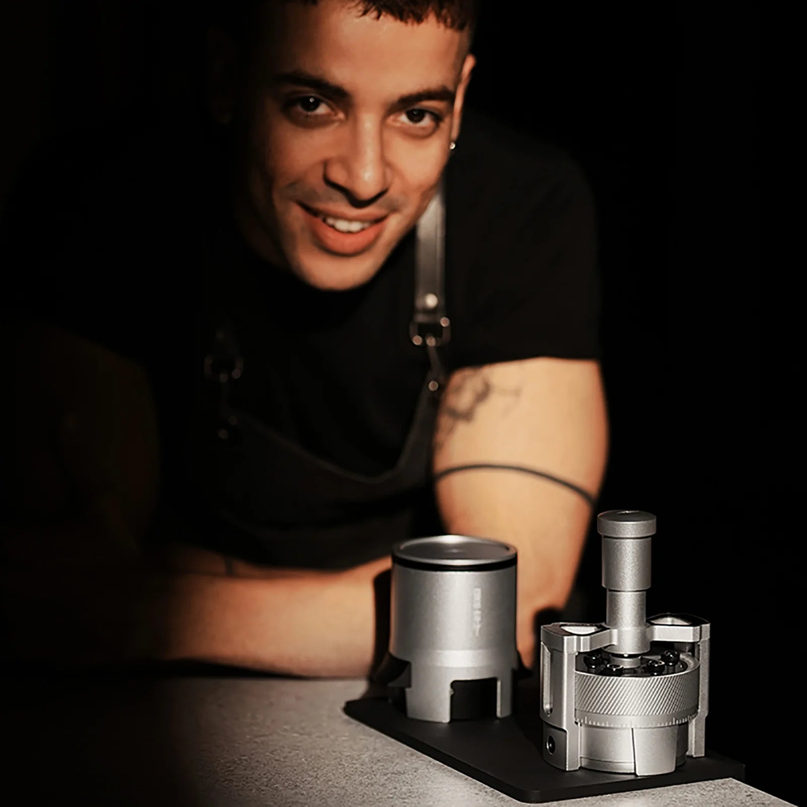 MHW-3BOMBER SE Pro espresso shaker funnel in silver, designed for consistent dosing, sits on counter near smiling barista.