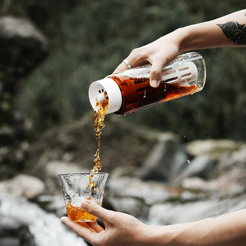 MHW-3BOMBER cold brew maker being poured. Clear Tritan bottle with white filter. Outdoors by river.