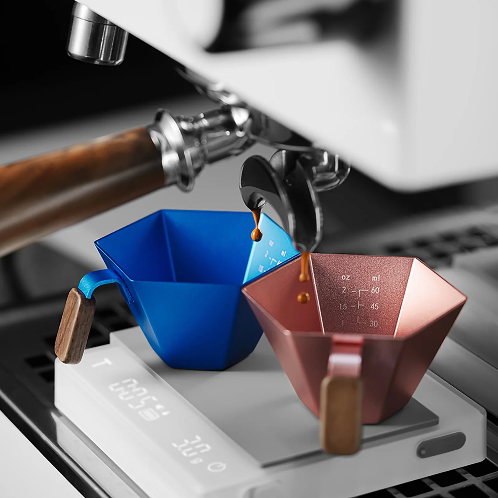 MHW-3BOMBER prism measuring cups in blue and copper with wood handles under an espresso machine. 
