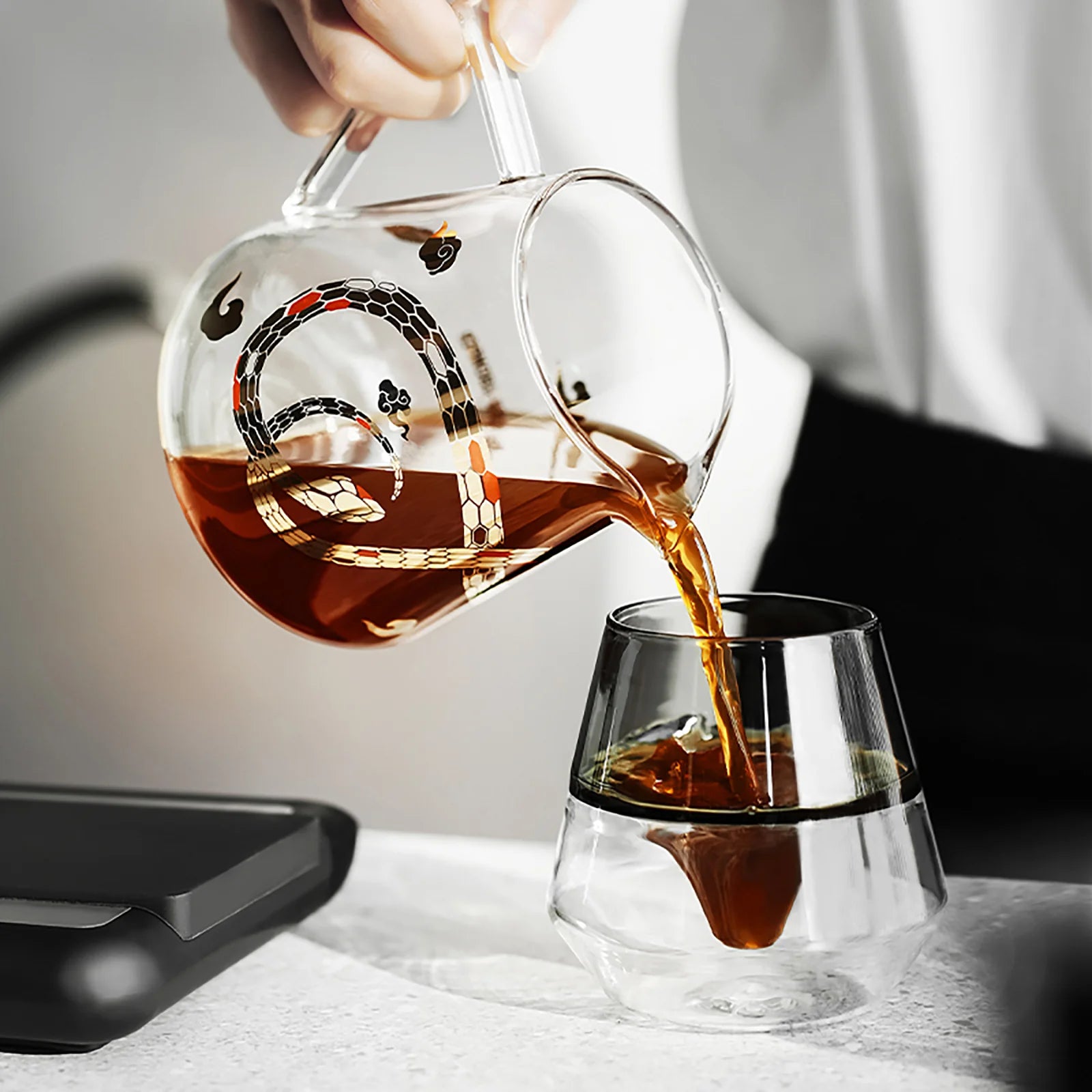 MHW-3BOMBER glass pitcher pouring tea into double-walled cup. Snake design. Heat-resistant. 