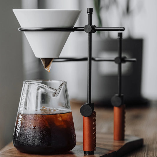 MHW-3BOMBER coffee dripper stand with white ceramic dripper, brown leather accents, and glass carafe. Making coffee.